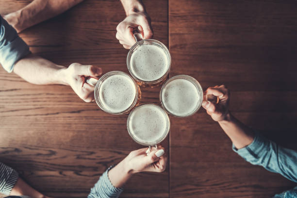 People holds mugs Cheers! Top view of people holding mugs with beer. pub table top view stock pictures, royalty-free photos & images