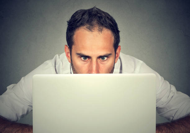 istock Surprised man with wide eyes hiding behind a laptop computer staring at the screen with a shocked scared face expression 685165688