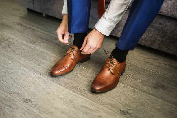 Photo of The man wears shoes. Tie the laces on the shoes. Men's style. Professions. To prepare for work, to the meeting.