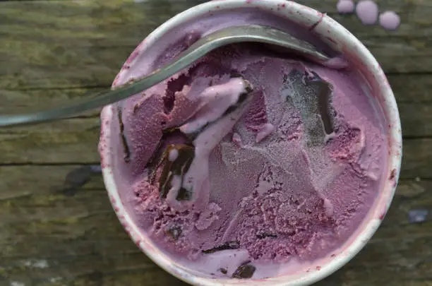 overhead view of a carton of black raspberry ice cream with chocolate chunks and spoon on wooden tabletop