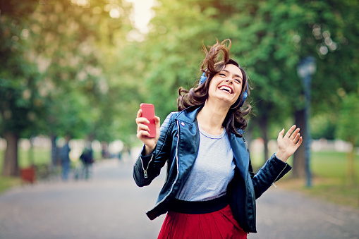 Young girl is dancing and listening the music till walking in the park