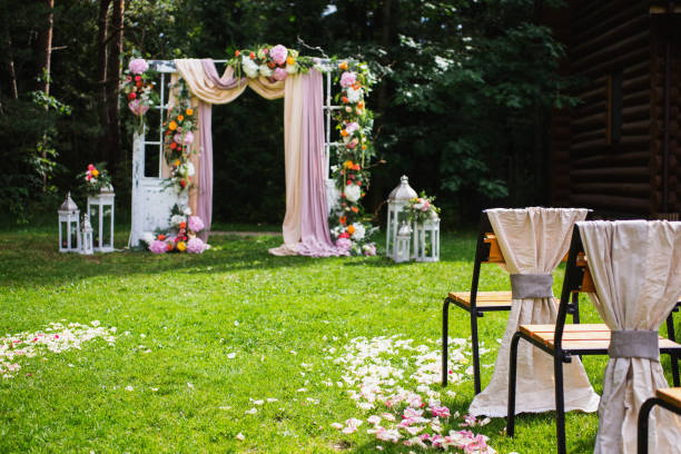 istock Beautiful wedding ceremony outdoors. Decorated chairs stand on the grass. Wedding arch made of cloth and white and pink flowers on a green natural background. Old doors, rustic style. 685212070