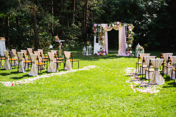 istock Beautiful wedding ceremony outdoors. Decorated chairs stand on the grass. Wedding arch made of cloth and white and pink flowers on a green natural background. Old doors, rustic style. 685212382