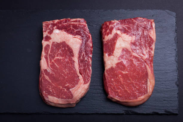 Two fresh raw marble meat, black Angus ribeye steak on a dark stone background