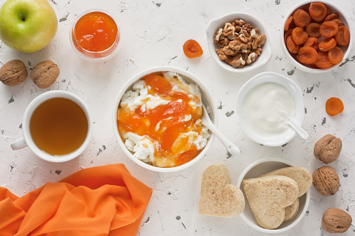 Cottage cheese with apricot jam, sour cream, yogurt, dried apricot, apple, walnut and cup tea with biscuits for healthy breakfast