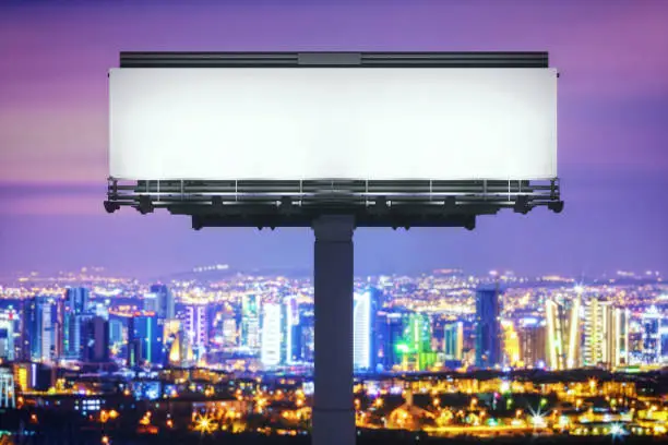 Blank large billboard against cityscape at night.