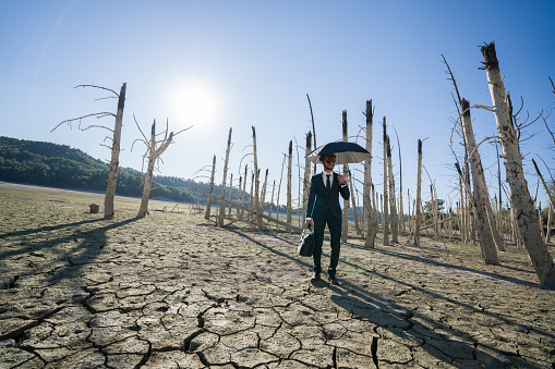 Businessman with umbrella standing on cracked earth waiting for the rain.