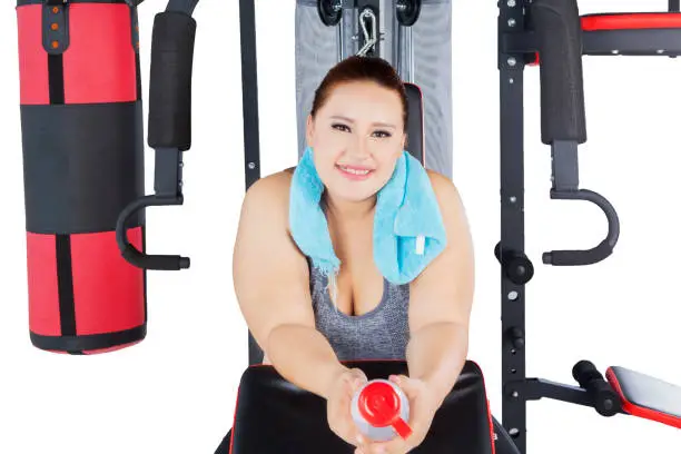 Beautiful overweight blonde woman smiling at the camera while sitting on gym equipment