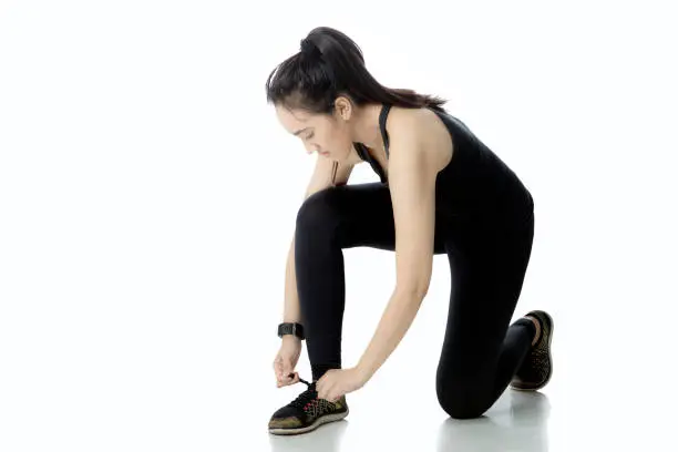 Young female wearing sportswear, tying her shoelaces with isolated on white background