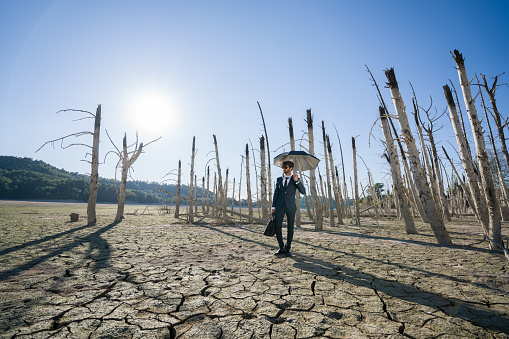 Businessman with umbrella standing on cracked earth waiting for the rain.