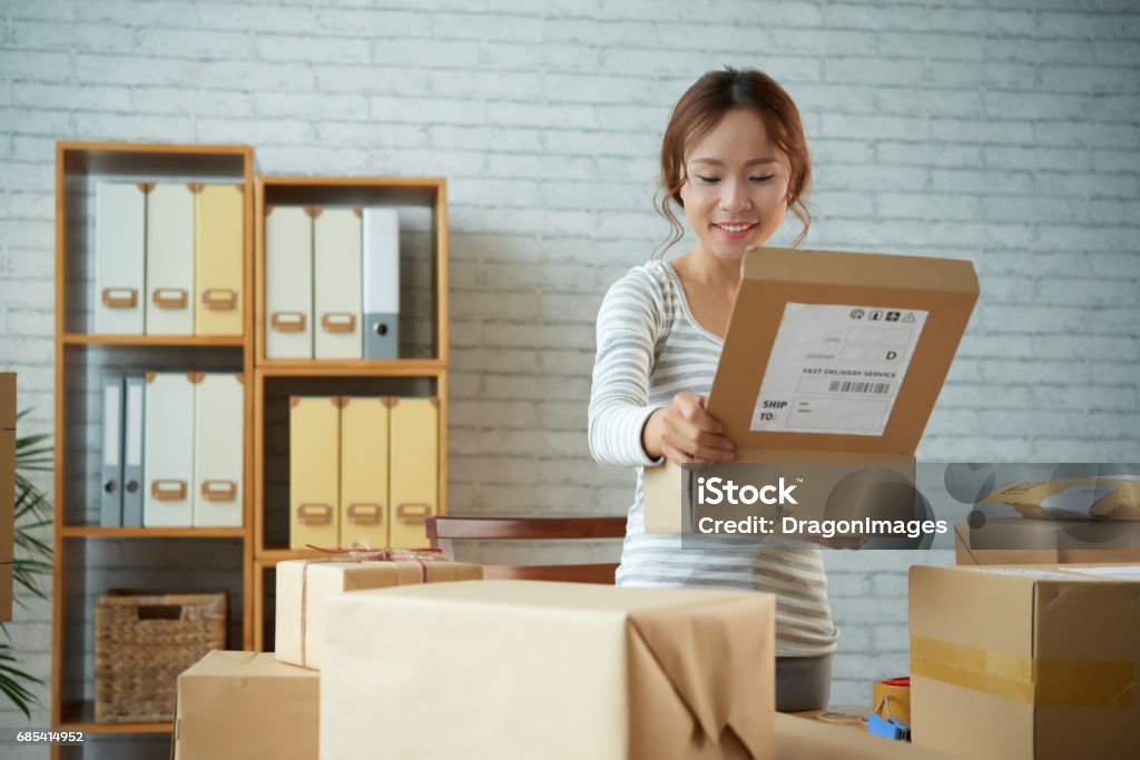 Opening parcel Happy Vietnamese young woman opening parcel she received Ordering Stock Photo