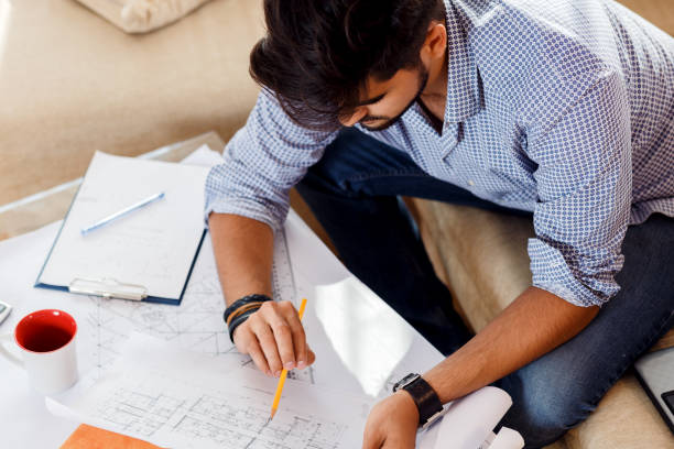istock Young businessman working at home. He sitting on sofa with laptop and looking at blueprints. 685425332