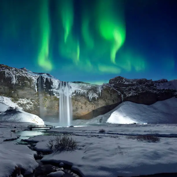 The Skogafoss waterfall and green aurora in midnight sky, Iceland.