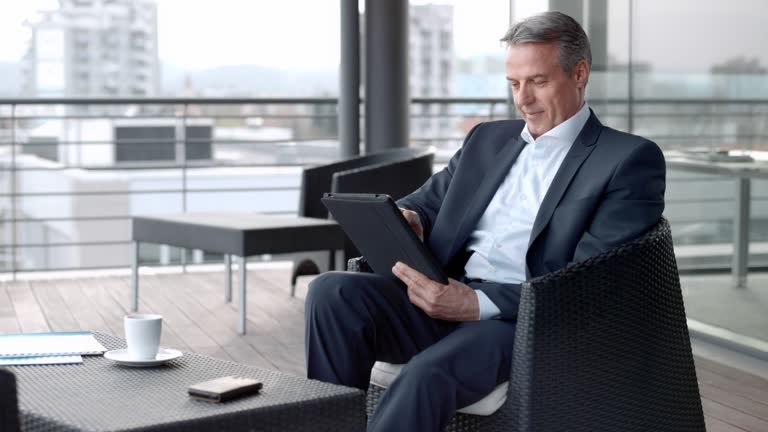 Senior Caucasian man working on the digital tablet while sitting in the terrace lounge in the city