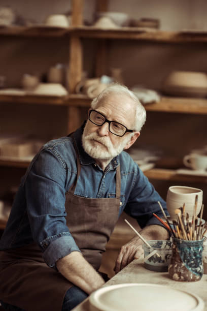 istock Senior potter in apron sitting at table and daydreaming at workshop 685464152