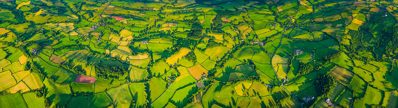 Aerial panoramic view over idyllic green landscape of patchwork pasture, meadows, agricultural crops and country villages.