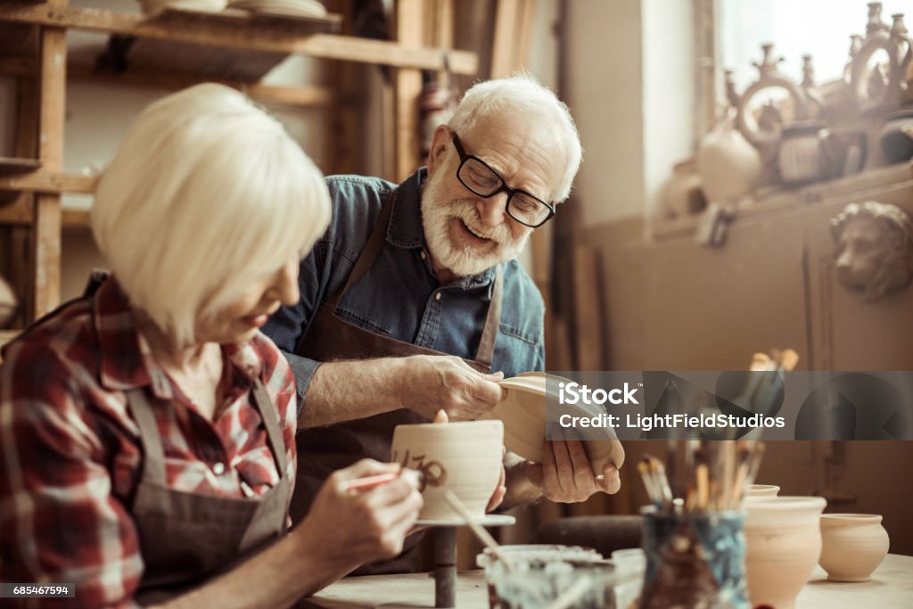 Woman painting clay pot with senior potter at workshop Hobbies Stock Photo