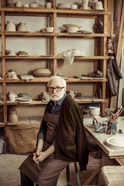 istock Senior potter in apron sitting at table and looking at camera at manufacturing 685470666