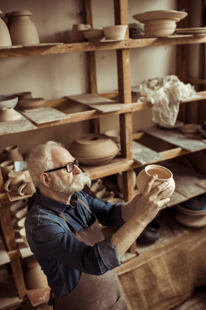 istock Senior potter in apron and eyeglasses examining ceramic bowl at workshop 685483784