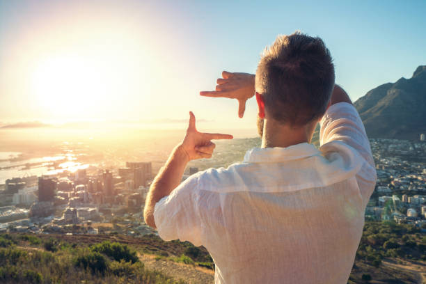 Young man framing sunrise with hands Young man relaxing by the sea at sunset framing the sunset with hands. Shot in Cape Town, South Africa. hand cropping photos stock pictures, royalty-free photos & images