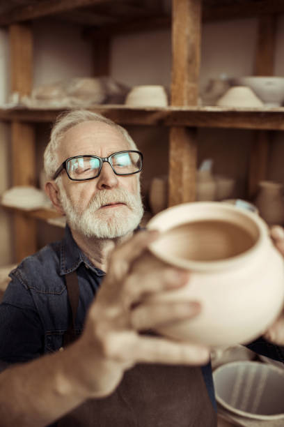 istock Senior potter in apron and eyeglasses examining ceramic bowl at workshop 685484470