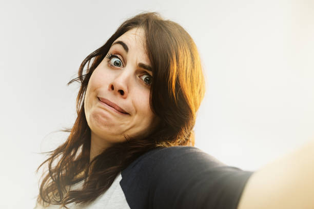 Portrait of young woman making a funny face and taking selfie. Horizontal shot of real woman against gray background.  Studio photography from a DSLR camera. Sharp focus on eyes.