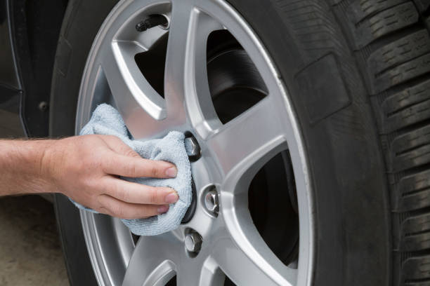 mão do homem com pano que limpa um disco empoeirado da roda de carro na garagem. lavagem adiantada da mola ou lavagem regular acima. lavagem de carro profissional pelas mãos. - alloy wheel - fotografias e filmes do acervo