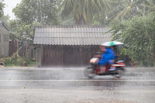 Motorcycle motion riding thourgh gale rain on front wooden house in road community