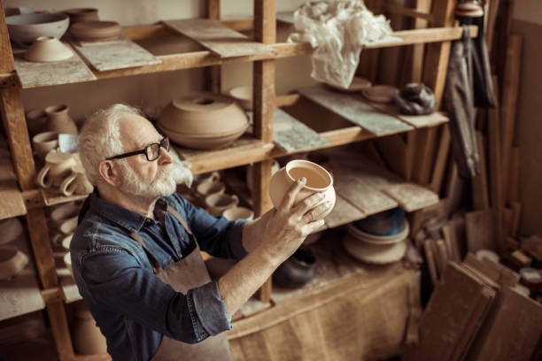 istock Senior potter in apron and eyeglasses examining ceramic bowl at workshop 685498182