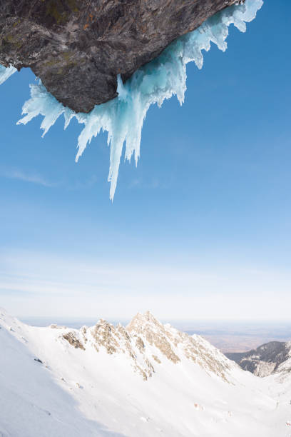 Sharp icicles hanging on craggy cliff with beautiful snow-capped mountain range scenery in background