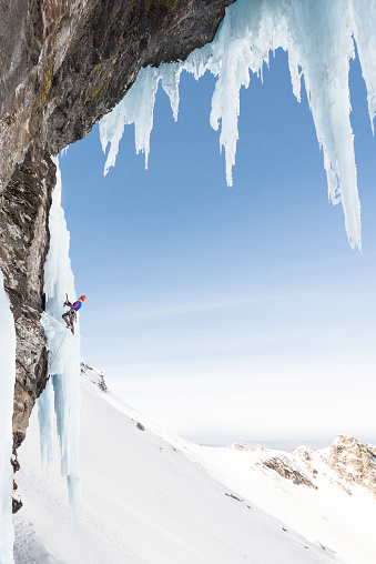Anonymous man ice climbing on sharp icicle hanging on frozen rock wall