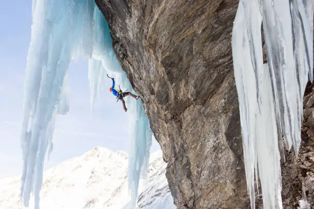 Anonymous man ascending on massive icicles using ice climbing gear