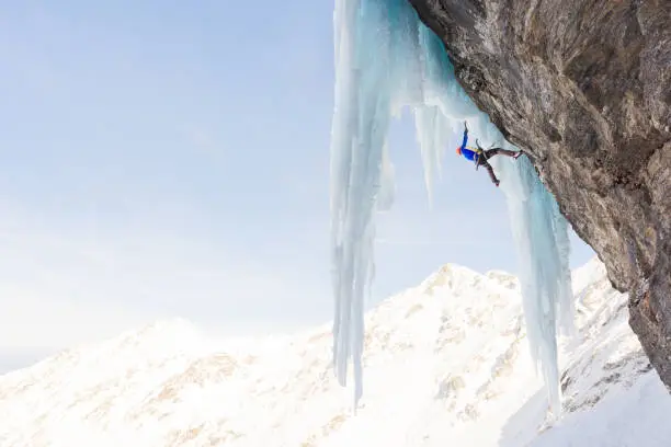 Low angle view of male alpinist ice climbing on massice icicles using ice axes