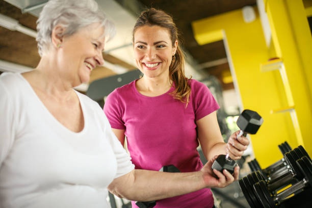 Personal trainer working exercise with senior woman in the gym. Woman picking weight. Workout in gym stock photo