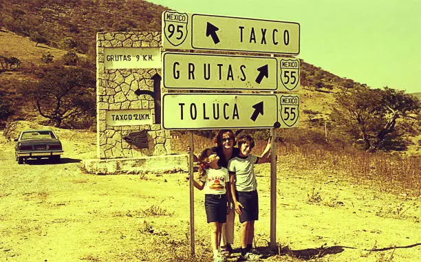 Vintage image of a family on a road trip to mexico standing besides directional signs.
