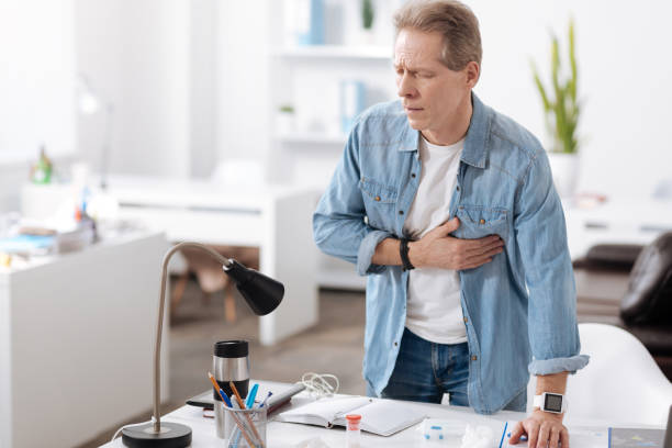 Anxious man having heart attack Call for help. Inactive male standing behind his workplace putting left hand on the table while touching his heart bronchiole stock pictures, royalty-free photos & images