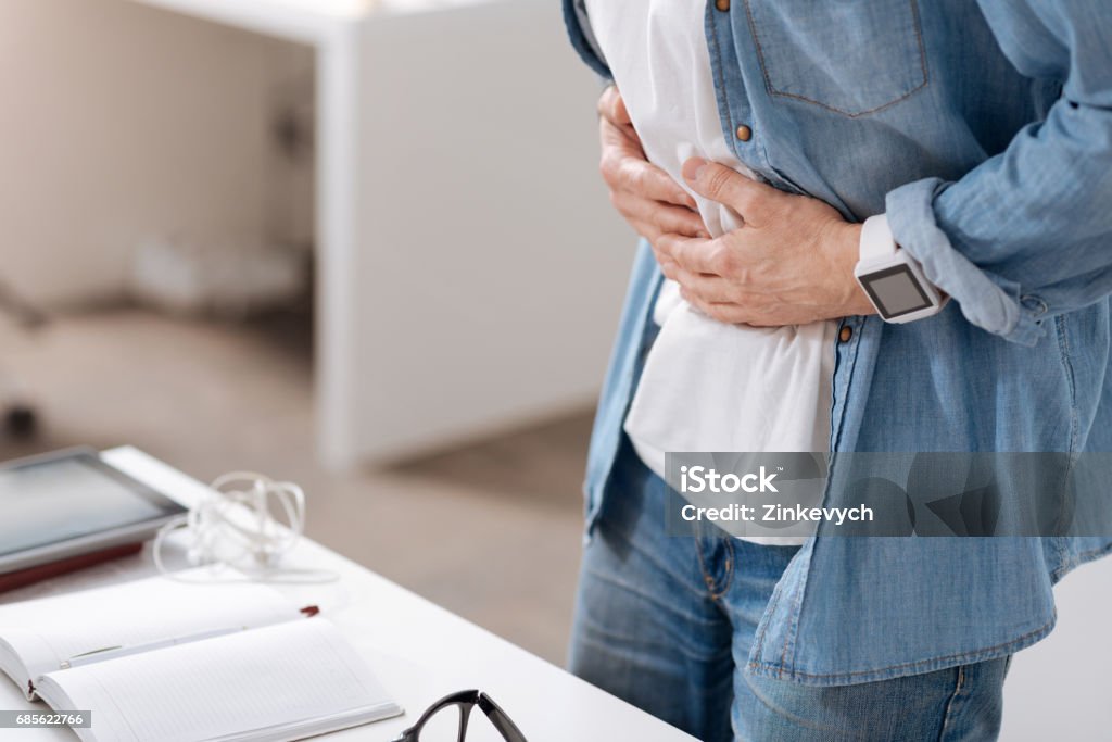 Photo of male having pain in belly Recommend medicine. Office worker wearing casual clothes putting hands on stomach while standing in semi position behind workplace Stomachache Stock Photo