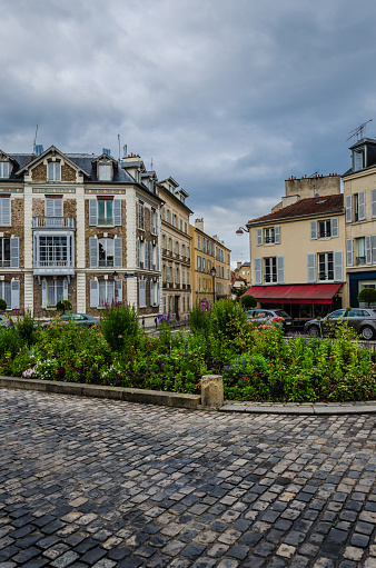 In the photo visable is a cobblestones and a flowerbed, in the back visable are romantic house facades and a sidewalk cafe.