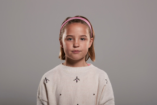 Portrait of a smiling little girl with flamboyant redhead and a turquoise glasses. She has curly hair and is looking at the camera. Light gray background. Focus on eyes. Horizontal indoors head and shoulders shot with copy space. This was shot in Quebec, Canada.