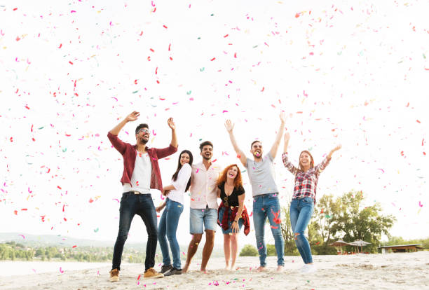 grupo de jóvenes celebrando en la playa - celebraciones públicas fotografías e imágenes de stock