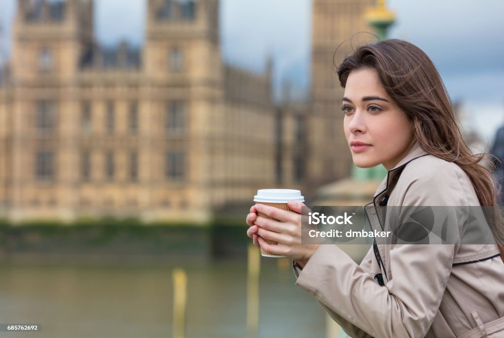 Beautiful sad, depressed or thoughtful young woman in London on Westminster Bridge over the River Thames drinking takeout coffee by Big Ben London - England Stock Photo