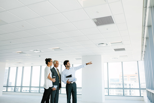 Real estate broker showing office space to clients. Business people and real estate agent at empty office space, with estate broker pointing at something interesting.