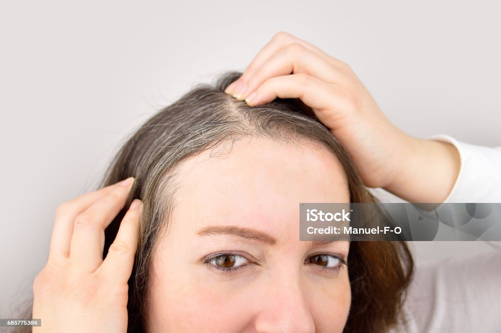 Young woman shows her gray hair woman is checking white hair while looking at the mirror White Hair Stock Photo