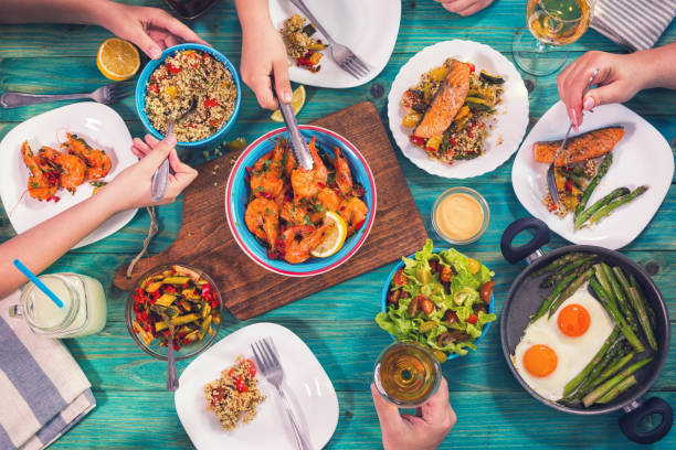 Young Family Having Lunch at Home Young family having lunch at home. On the table are seafood,grilled salmon, couscous, grilled shrimp, asparagus with eggs and salad eating asparagus stock pictures, royalty-free photos & images