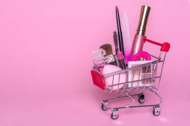 Shopping trolley with makeup on a pink background. Perfume, brush, mascara