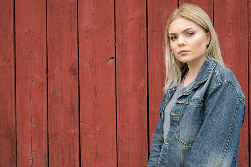 Portrait of beautiful blonde Scandinavian teenage girl against red traditional wooden building wall at Turku Finland