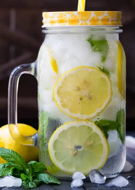 Sassy water. Slices of lemons with mint in the mason jar filled with water and ice. Healthy water with mint, sliced lemons and cucumbers. Lemons pattern. Lemonade.