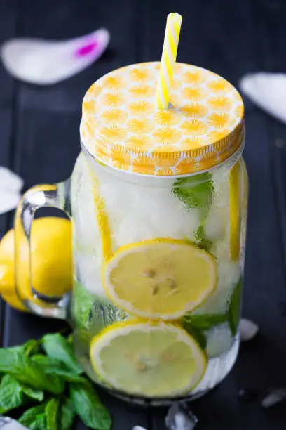 Sassy water. Slices of lemons with mint in the mason jar filled with water and ice. Healthy water with mint, sliced lemons and cucumbers. Lemons pattern. Lemonade.