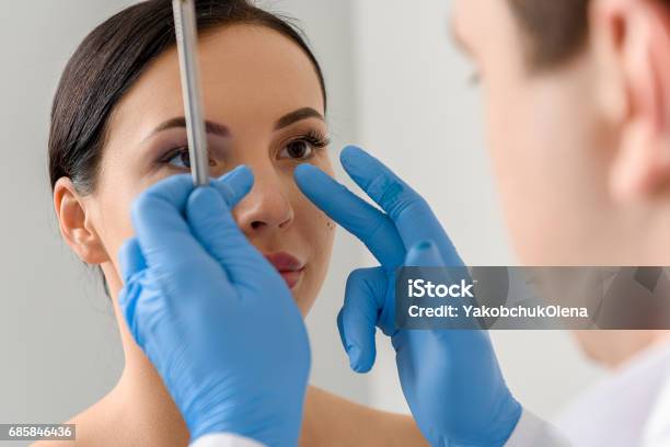 Physician Examining Face Of Serene Female Stock Photo - Download Image Now - Nose, Plastic Surgery, Surgery