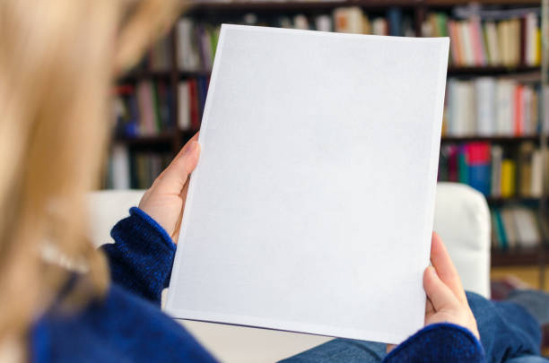 блондинка сидит дома на диване и держит в руках пустую брошюру - notebook book paper note pad стоковые фото и изображения